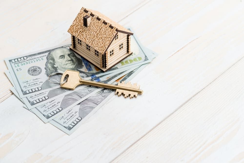 Wooden model house and brass key on US $100 bills.
