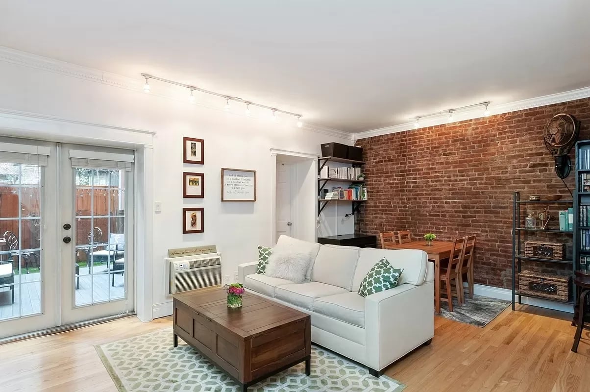 Living room with a white sofa, exposed brick wall, hardwood floors, and French doors to a patio.