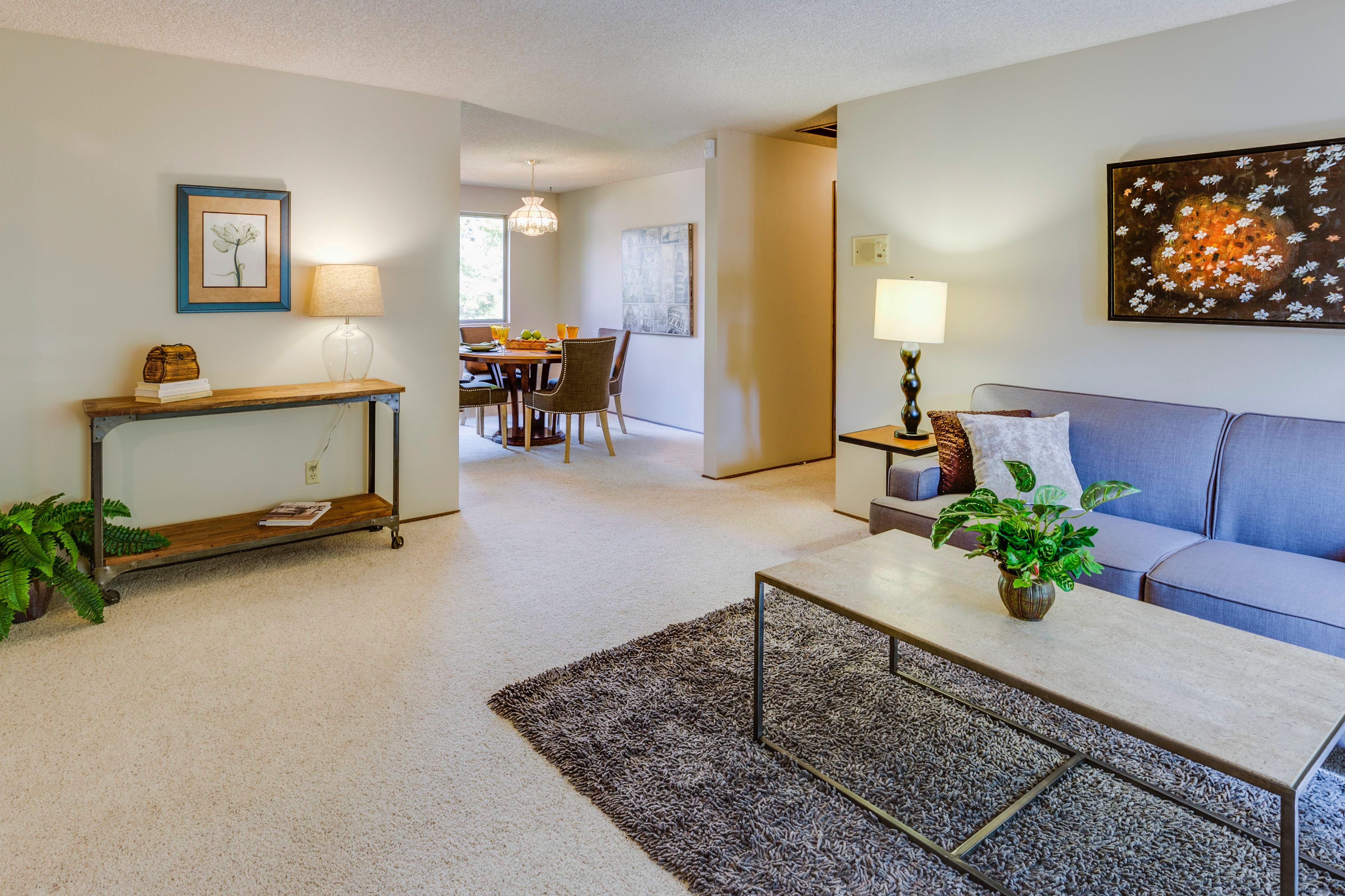 Furnished living room with a blue sofa, textured rug, and dining area beyond.