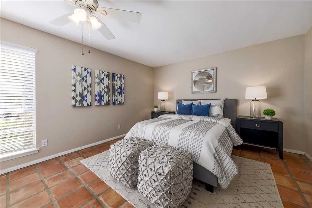 Staged bedroom with blue pillows, patterned bedding, and terracotta tile flooring.