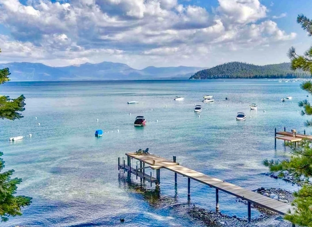 Lake Tahoe with anchored boats, a wooden pier, and forested mountains across the water.