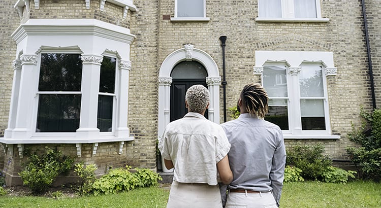 A couple standing in front of a house, looking at it together.