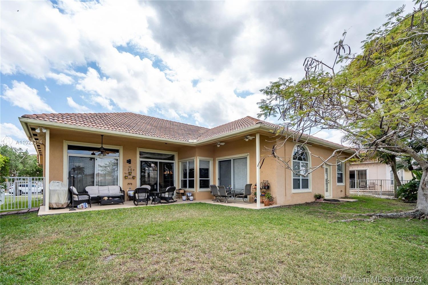Home’s rear exterior with a covered, furnished patio and grassy yard.