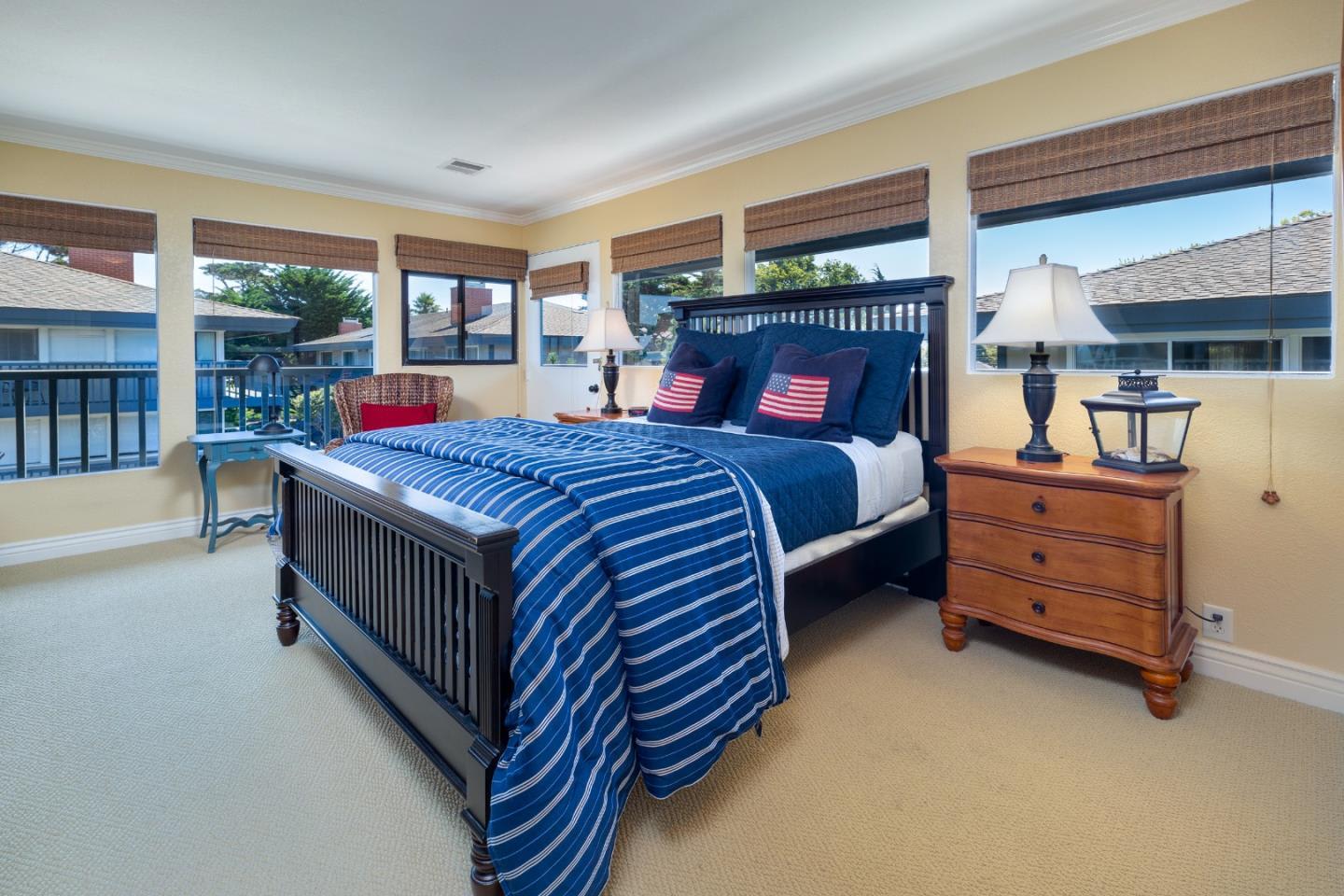 Bedroom with blue striped bedding, flag pillows, and multiple windows with woven shades.