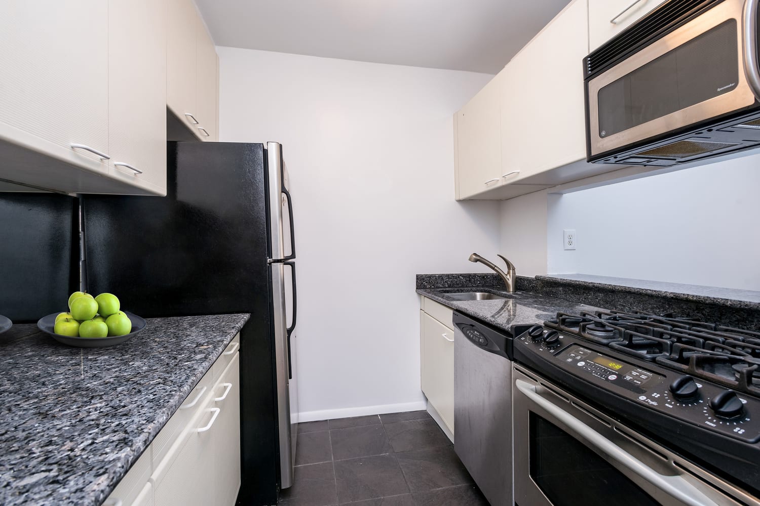 Apartment kitchen with granite counters, black refrigerator, and stainless-steel gas range.