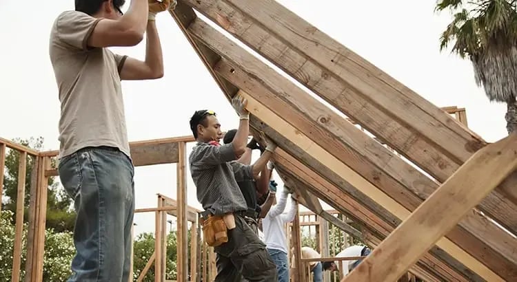 A group of people working together to build a wooden structure, possibly a house frame, suggesting teamwork and construction.