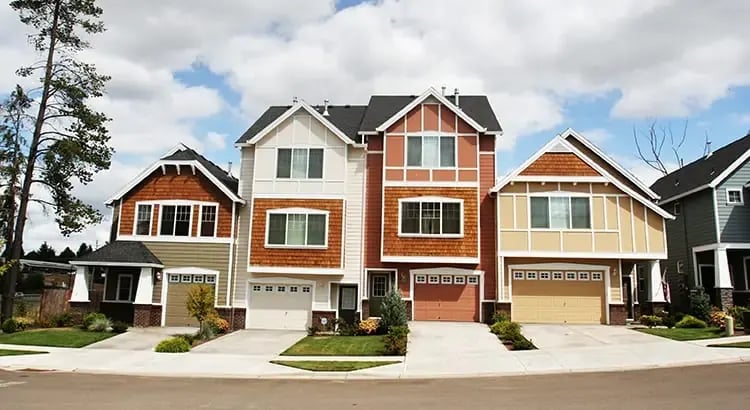 An exterior view of a row of new, modern houses. The houses have a similar architectural style, with different colors and features, and are set against a partly cloudy sky.