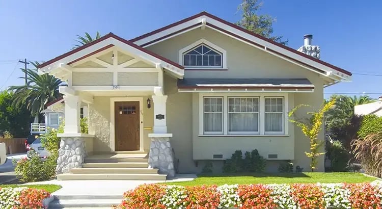 A beautiful house with a well-maintained garden and a clear blue sky. The house has a welcoming front porch and is surrounded by vibrant flowers.