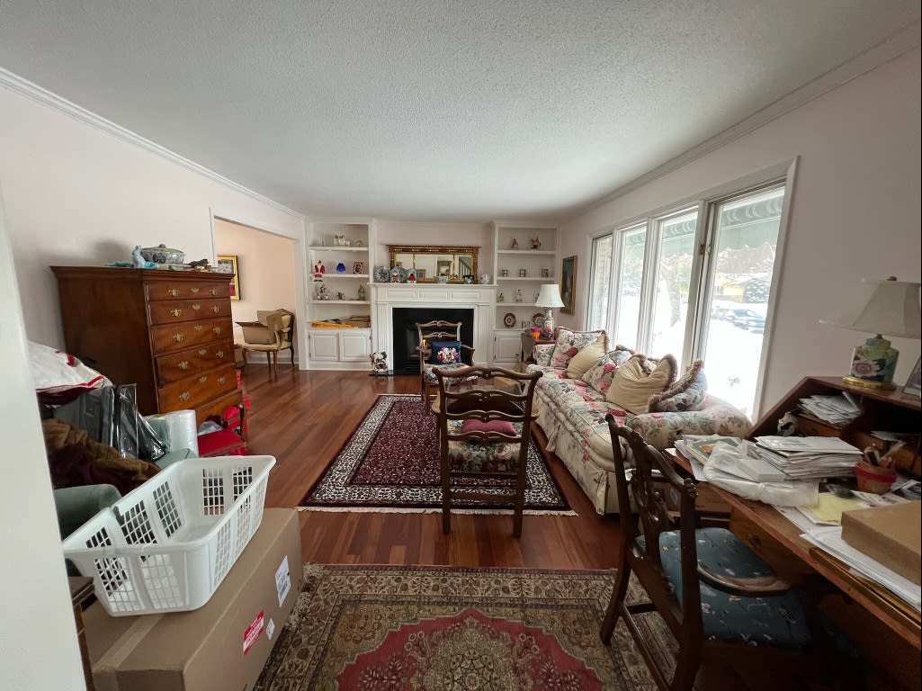 A living room with a couch, chairs, a fireplace, and a cluttered desk in the corner.