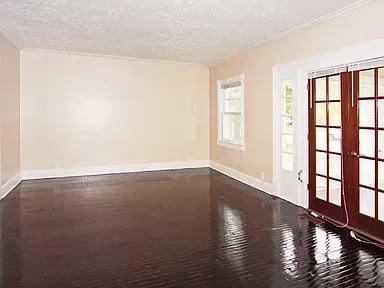 Empty room with glossy dark hardwood floors and dark wood French doors.
