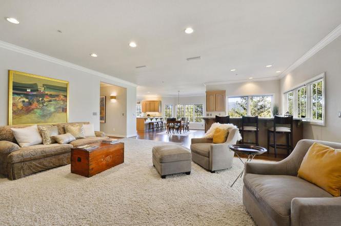 Furnished living room with neutral seating, a wooden chest coffee table, and windows overlooking greenery.