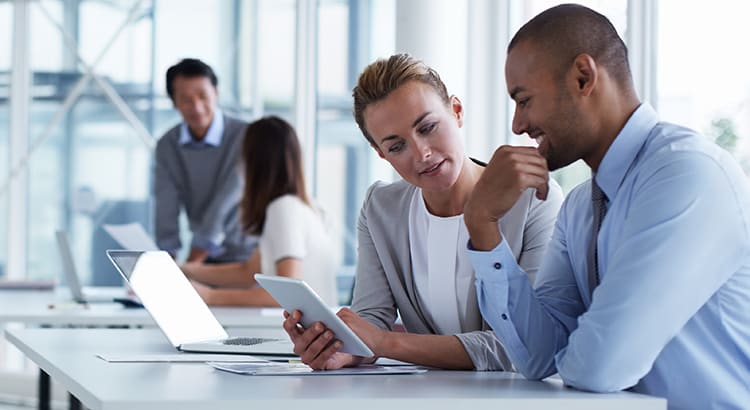 People in a business setting, looking at a tablet together. They appear to be discussing something related to financial or real estate matters.