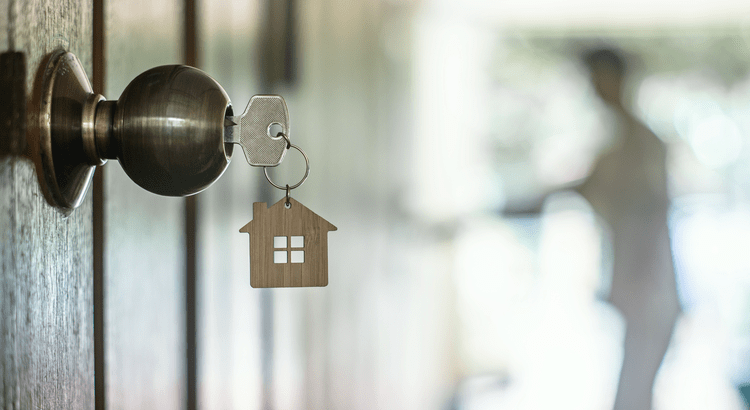 A key with a house-shaped keychain in a door lock, likely related to home buying or renting.