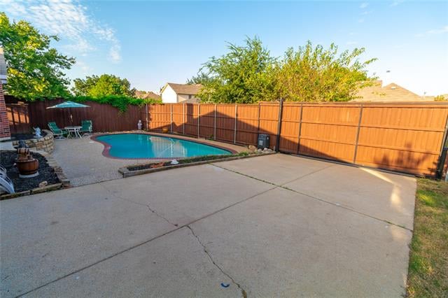 Backyard pool beside a broad concrete patio, enclosed by a wooden privacy fence.