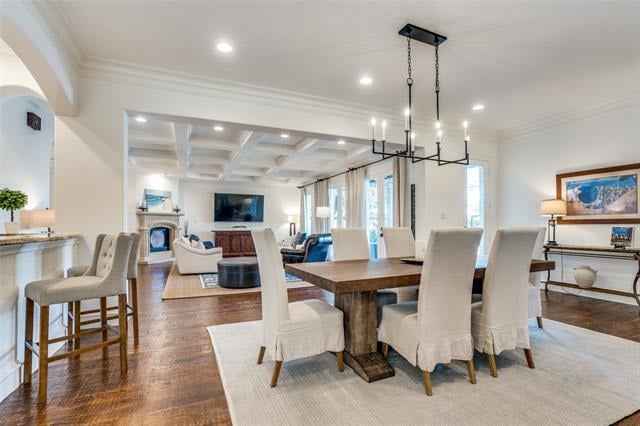 Open dining room with a rustic wood table, upholstered chairs, and a black chandelier beside the living area.
