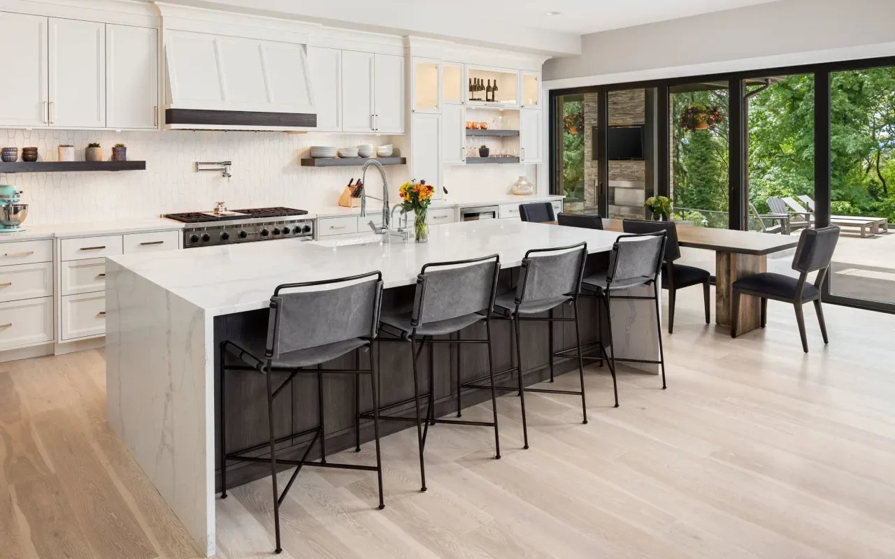 Modern kitchen island with waterfall countertop and sleek bar stools, bathed in warm light.