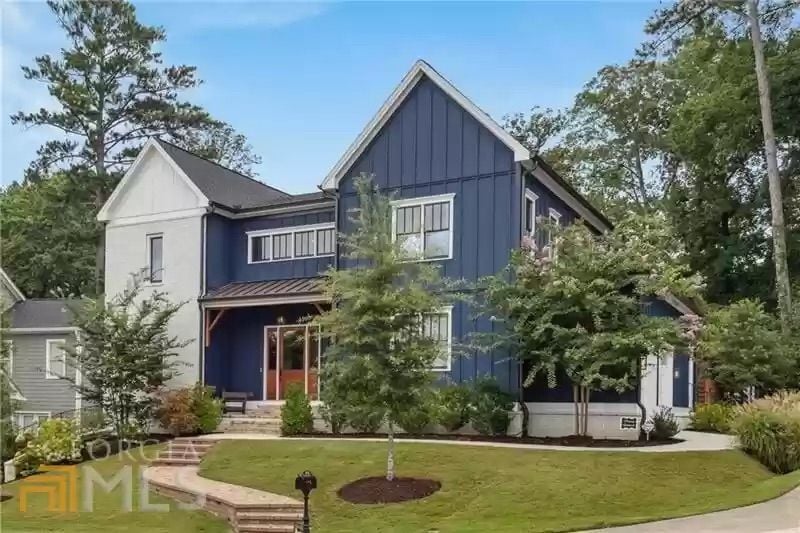 Blue two-story house with white trim, a covered entry, mature trees, and a landscaped front yard.