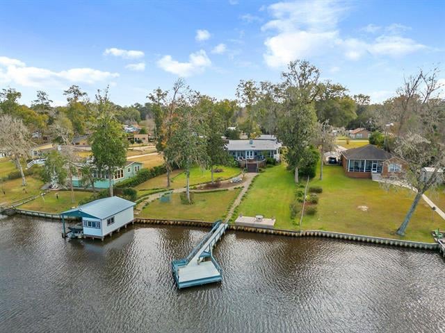 A aerial view of 24230 Jesse Ave property located by the water, featuring a dock and a boat. The house is situated on a grassy lawn with trees in the background, suggesting a scenic and tranquil setting.