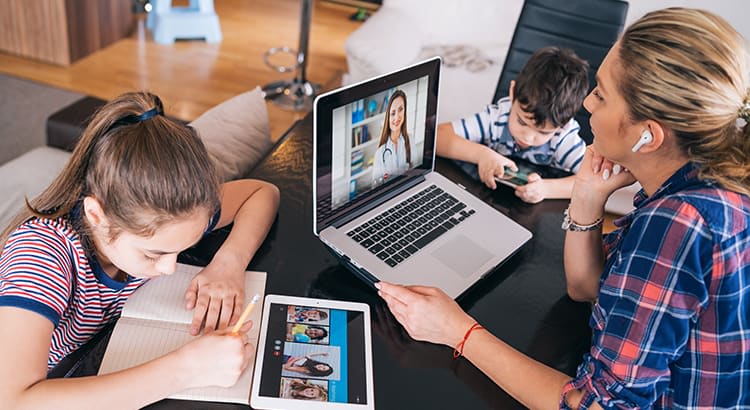A woman and her child are sitting at a table, involved in a virtual meeting, with multiple devices and screens open, likely symbolizing remote work, family life, and technology.