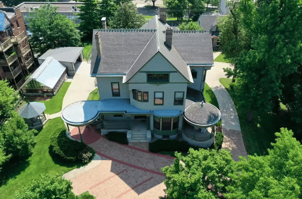 Aerial view of a gabled house with rounded porches and a brick driveway.