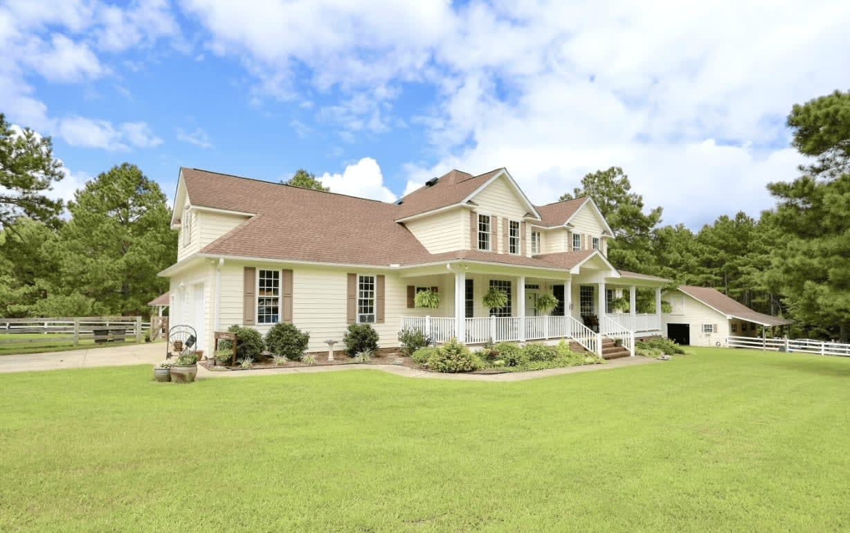 A luxurious white farmhouse nestled in a sprawling yard, radiating a tranquil ambiance.