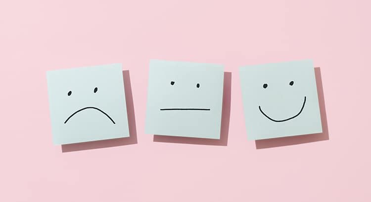 Three square sticky notes arranged in a horizontal line against a light pink background. Each sticky note features a simple black line drawing representing a different facial expression.