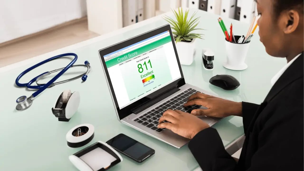 A person working on a laptop with a high credit score displayed on the screen. The setting is a modern office, indicating financial planning or monitoring.