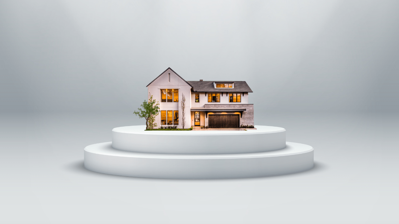 A miniature house model on a round pedestal, set against a neutral background. The house is well-lit and detailed, representing real estate or home ownership.