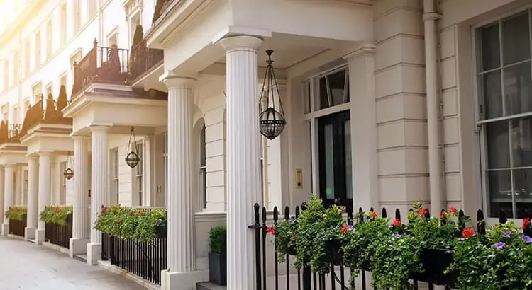 The exterior of a grand building with large columns and decorative railings. The setting appears to be a residential or institutional building with well-maintained landscaping.