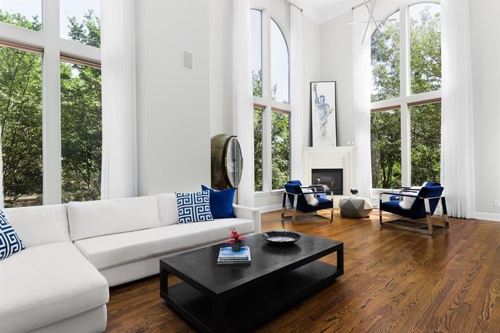 Living room with a white sectional, fireplace, hardwood floors, and tall windows overlooking trees.