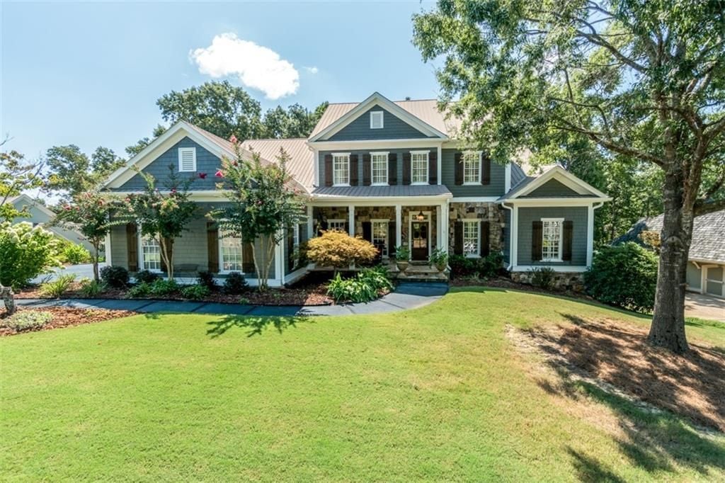 Blue-gray two-story house with a covered porch, stone accents, and a broad lawn.