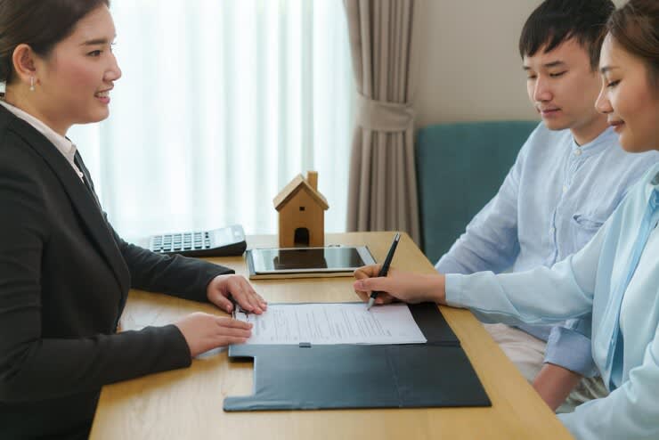 asian woman real estate agent with a couple signing for contract