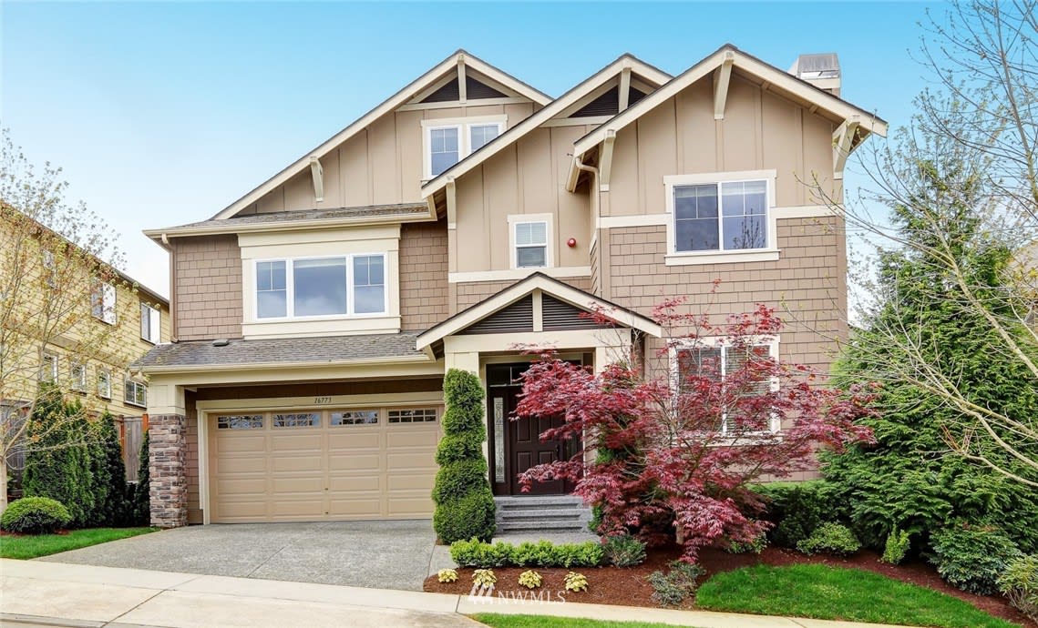 Two-story beige home with a double garage, covered entry, and red-leaf Japanese maple landscaping.