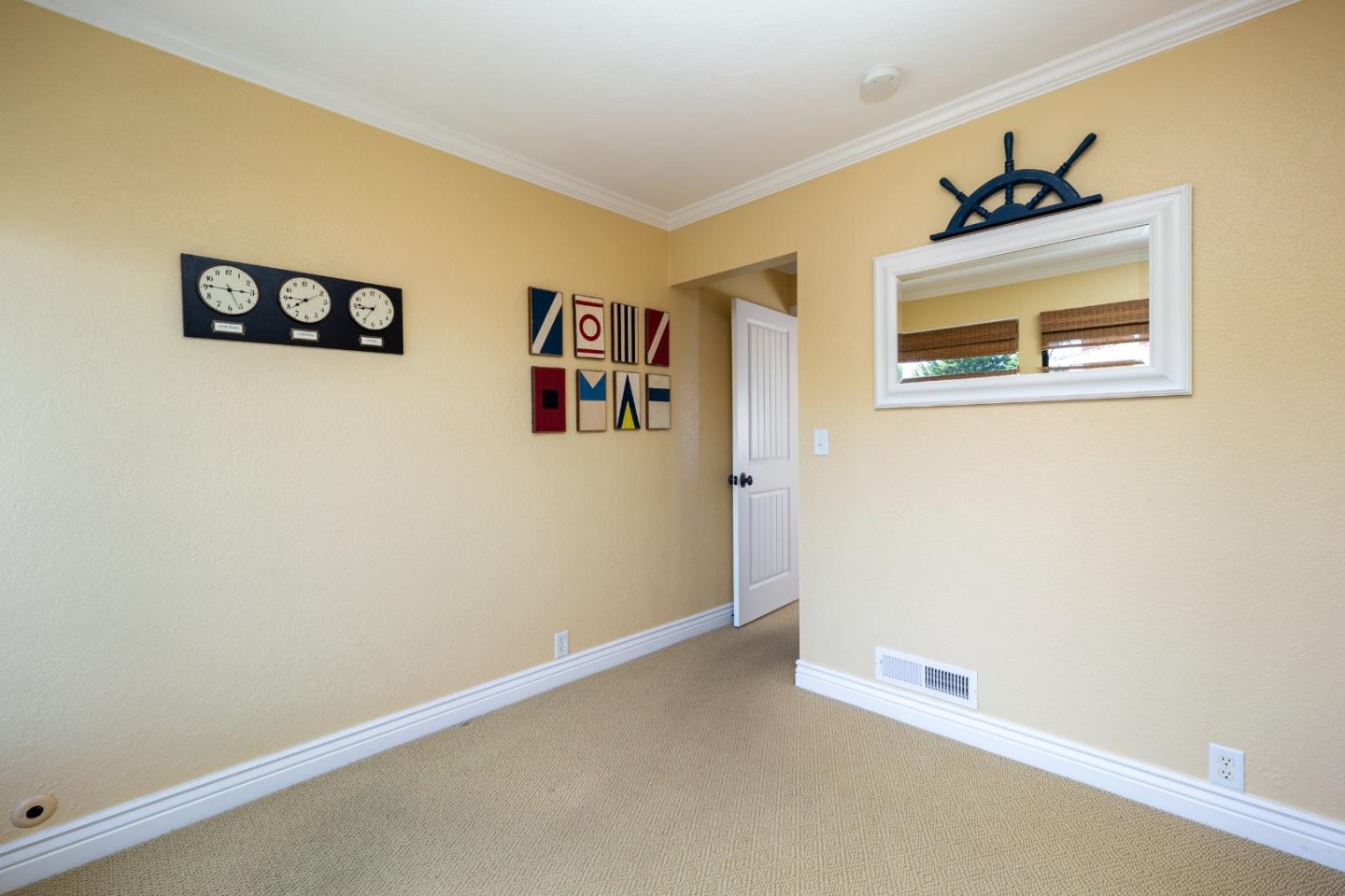 Empty carpeted room with pale yellow walls, nautical decorations, and a white-framed mirror.