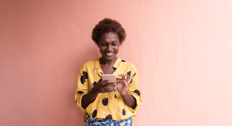 A woman using her mobile phone against a pink wall