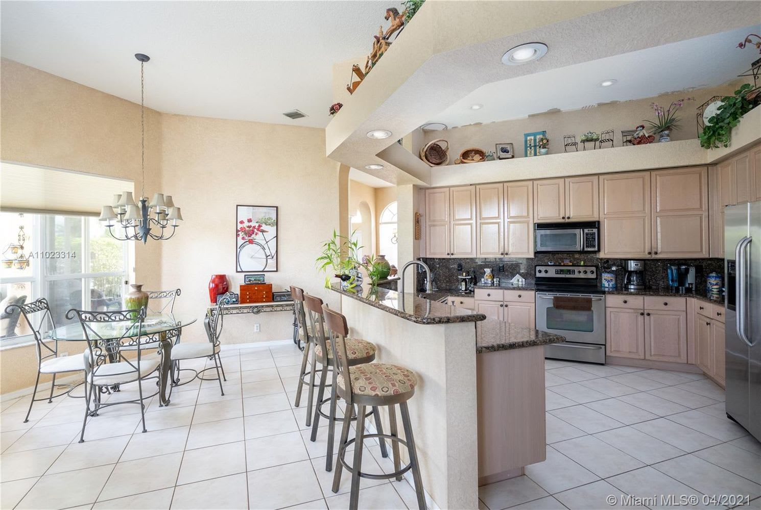 Kitchen and dining area with a granite breakfast bar, pale cabinets, and stainless steel appliances.