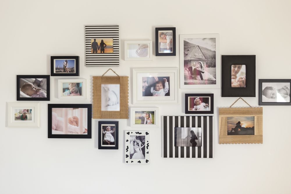 Gallery wall of family photos in mixed black, white, striped, and woven frames.