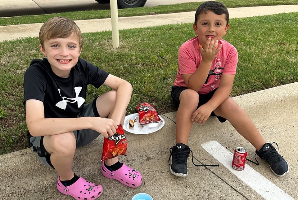 Young boys sitting on the sidewalk while eating chips