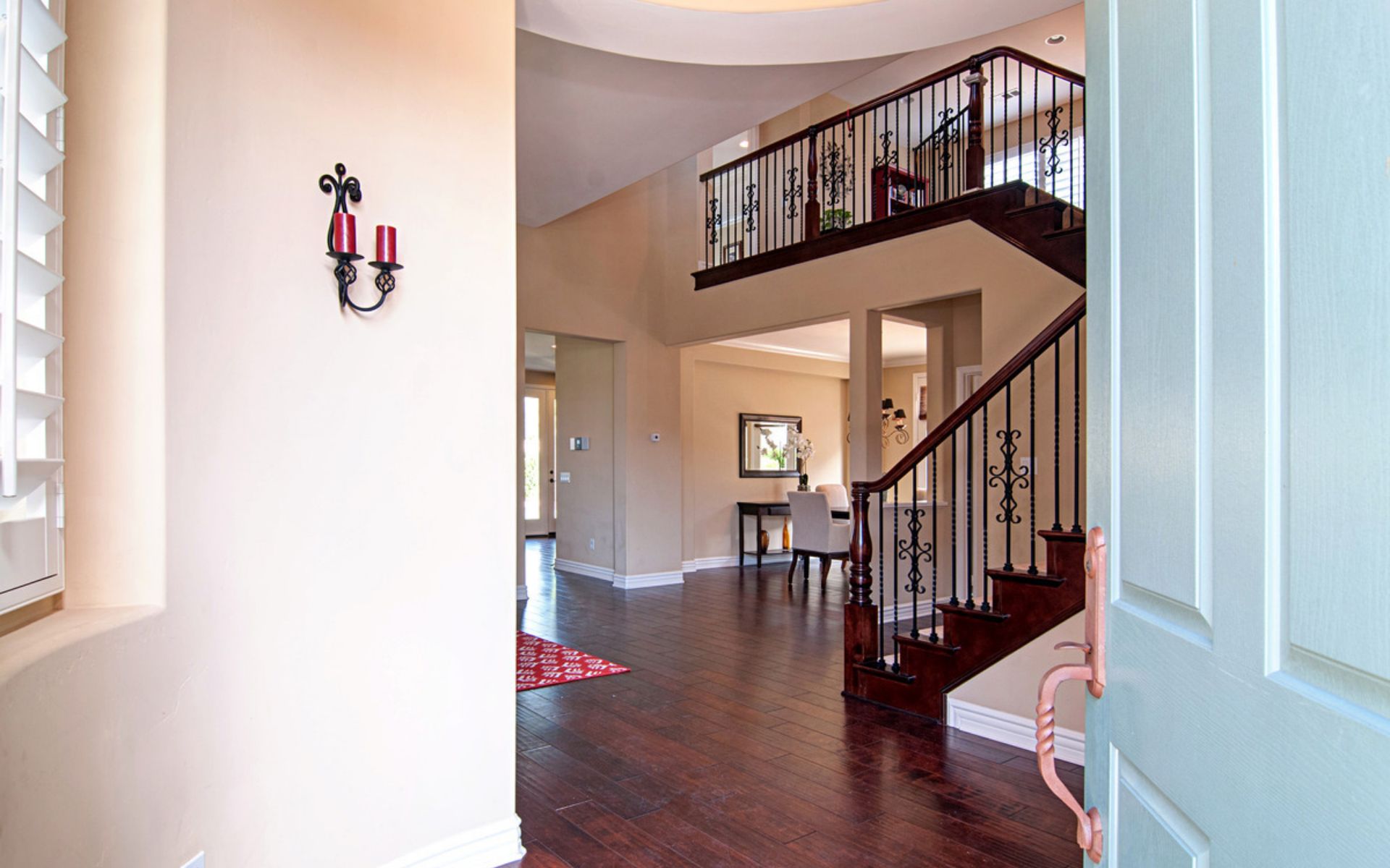 Foyer with dark wood floors and an ornate curved staircase beside the open front door.