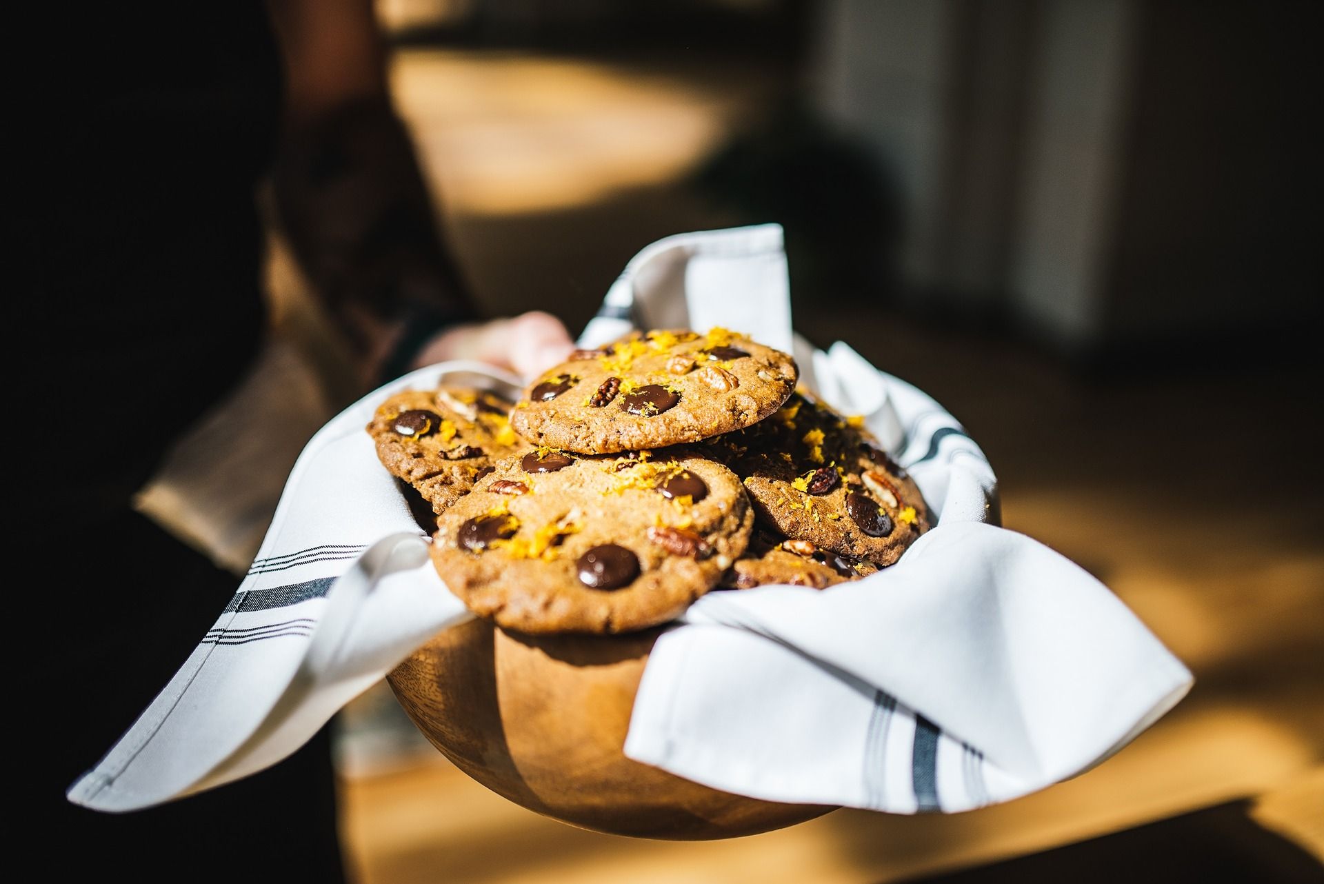 Chocolate chip cookies topped with nuts and orange zest in a cloth-lined bowl.