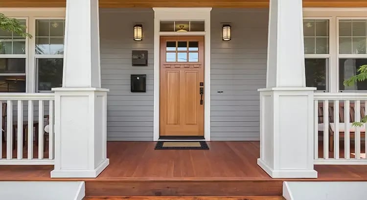 The front porch of a house with white columns and a wooden door. The entrance is inviting, with steps leading up to the porch and a well-maintained exterior.