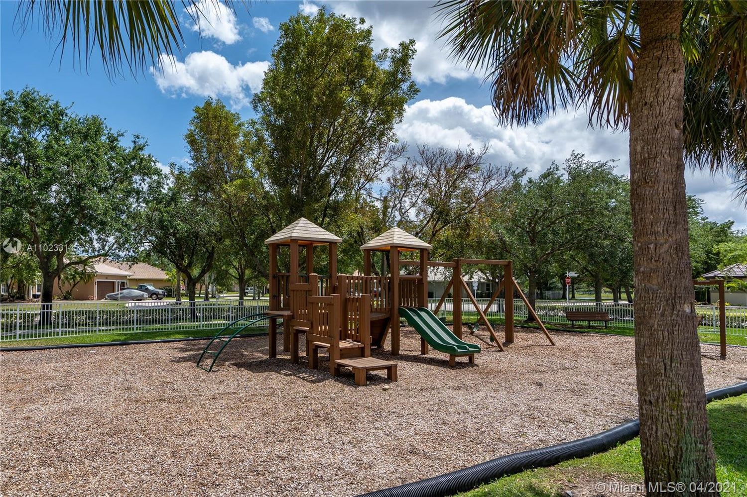 Community playground with a wooden play structure, green slides, and swings beneath mature trees.