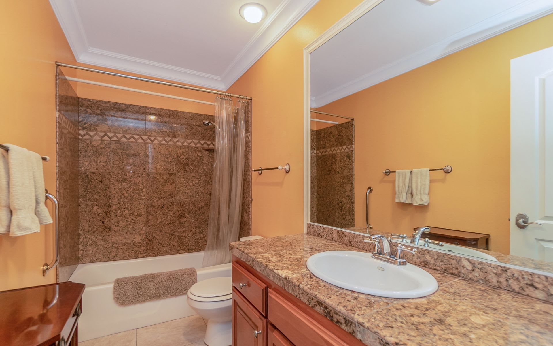 Bathroom with a stone-tile shower surround, large mirror, and wood vanity with granite-look countertop.