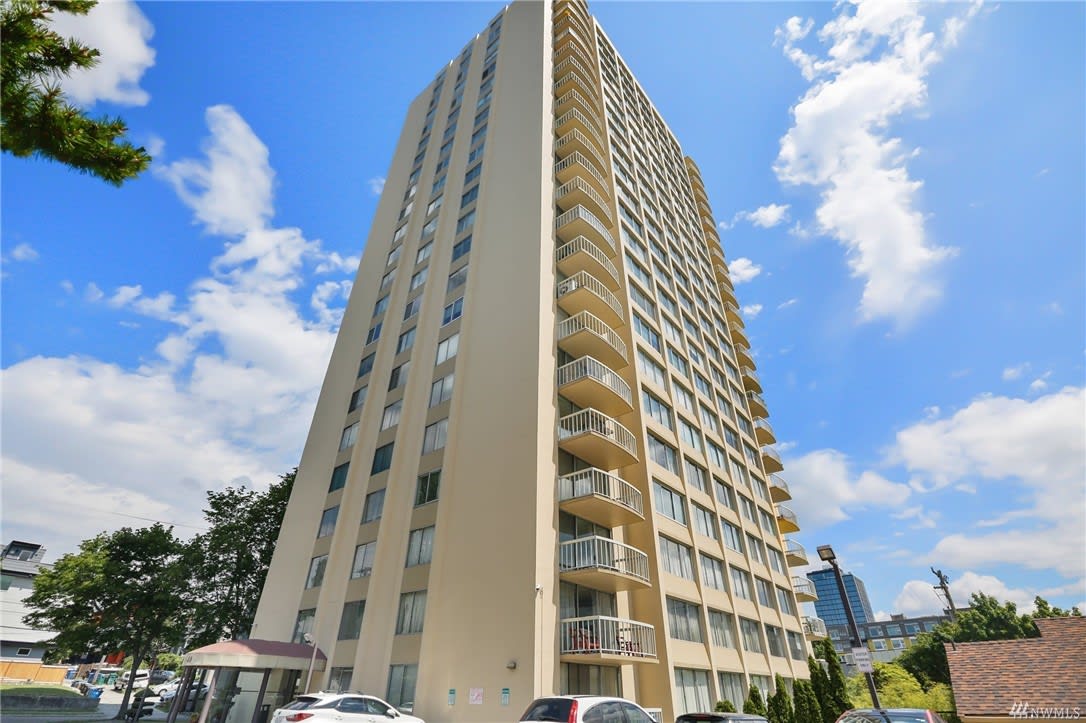 Modern high-rise condo against a blue sky, offering luxury urban living with convenient amenities nearby.