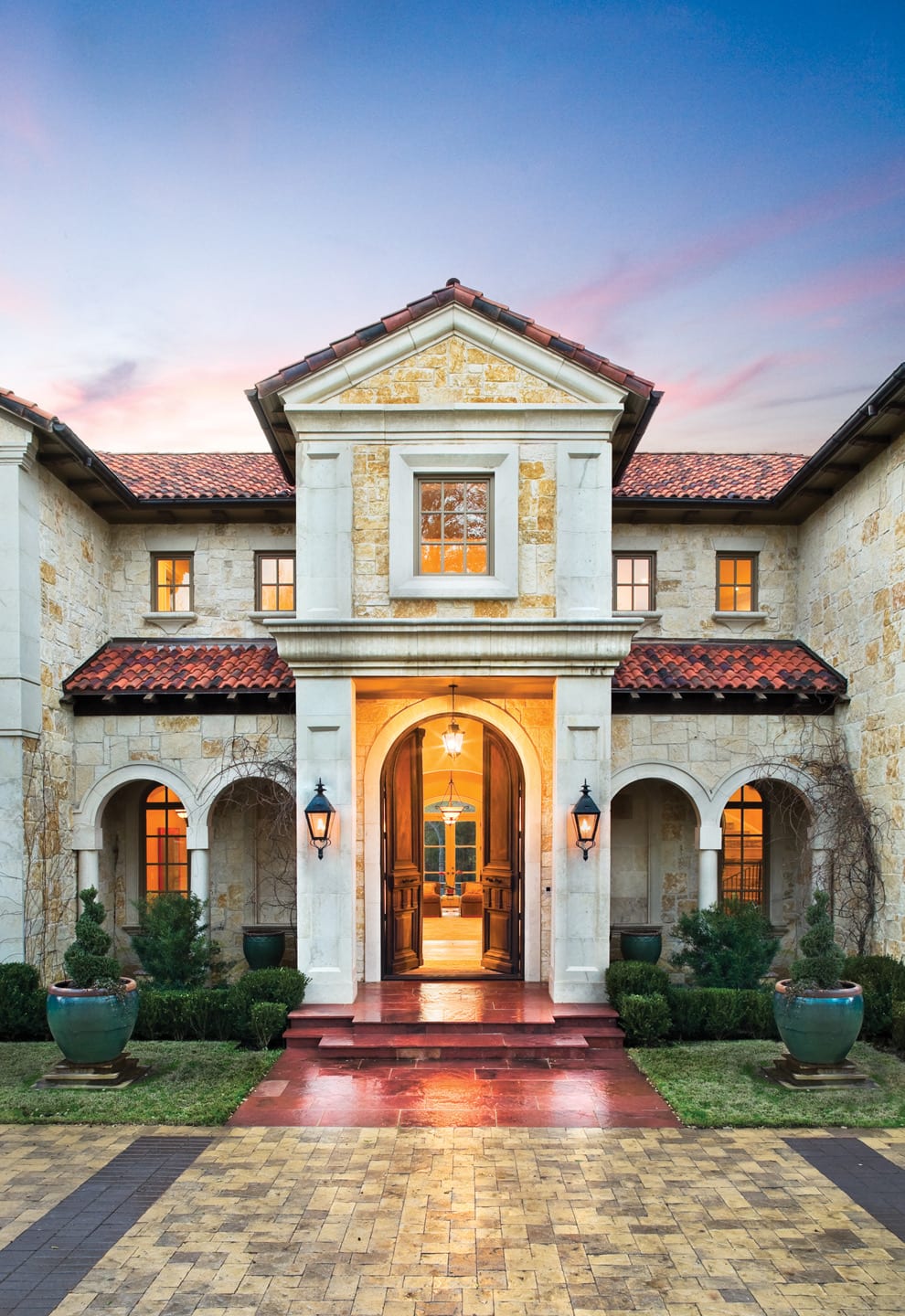 Stunning custom home exterior in Dallas, featuring Mediterranean architectural design with stone walls and arched entryways