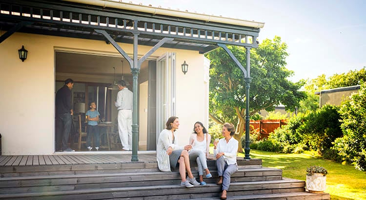 A family sitting on the porch of their house. They are enjoying a sunny day, indicating themes of homeownership, family life, and outdoor leisure.