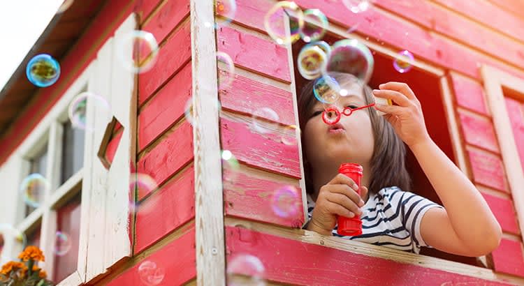 A child blowing bubbles outside of a red house, giving a playful and carefree feeling.