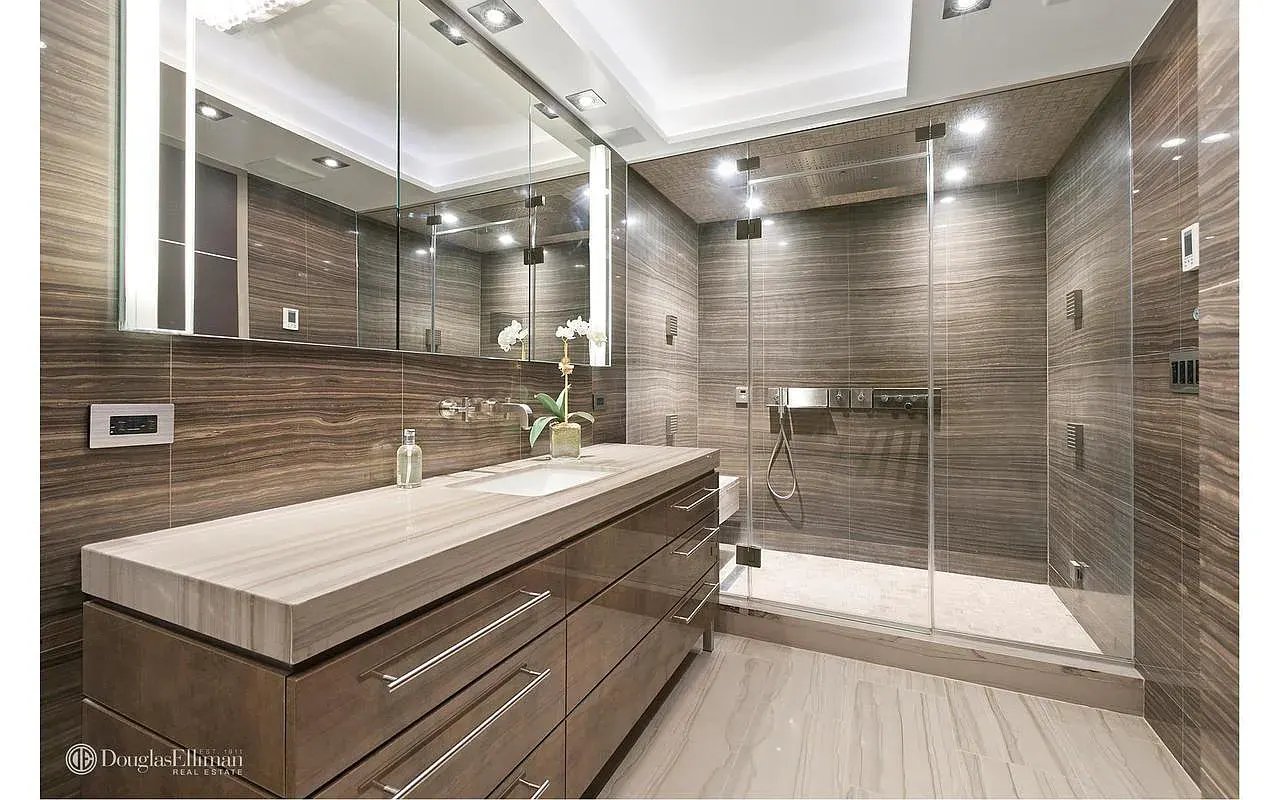 Modern bathroom with a long stone vanity, mirrored wall, and glass-enclosed shower.