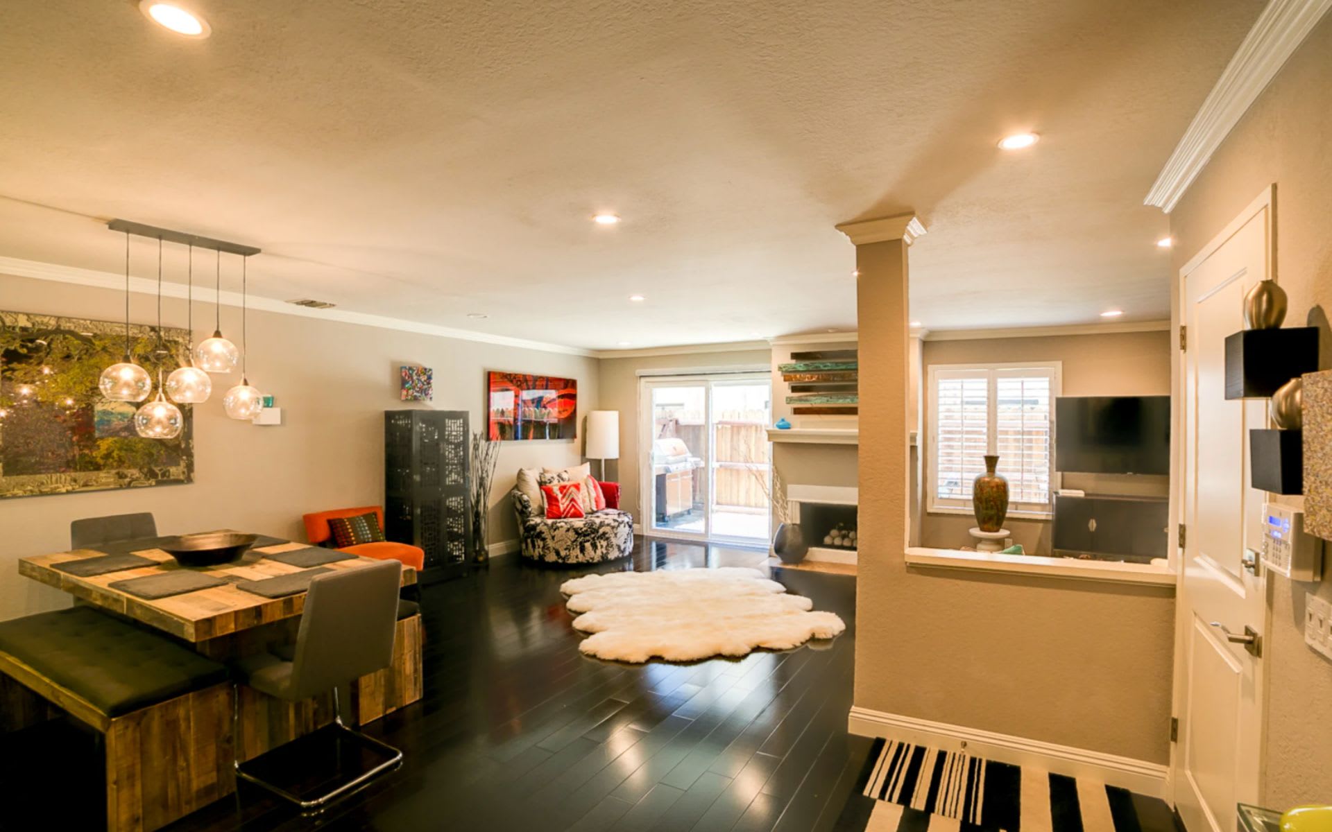 Open-plan living and dining room with dark wood floors, pendant lights, and sliding glass doors.