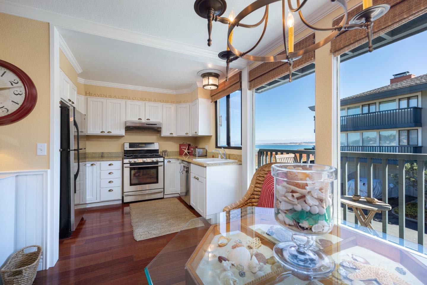 Kitchen with white cabinets and stainless appliances, opening to a balcony overlooking the ocean.